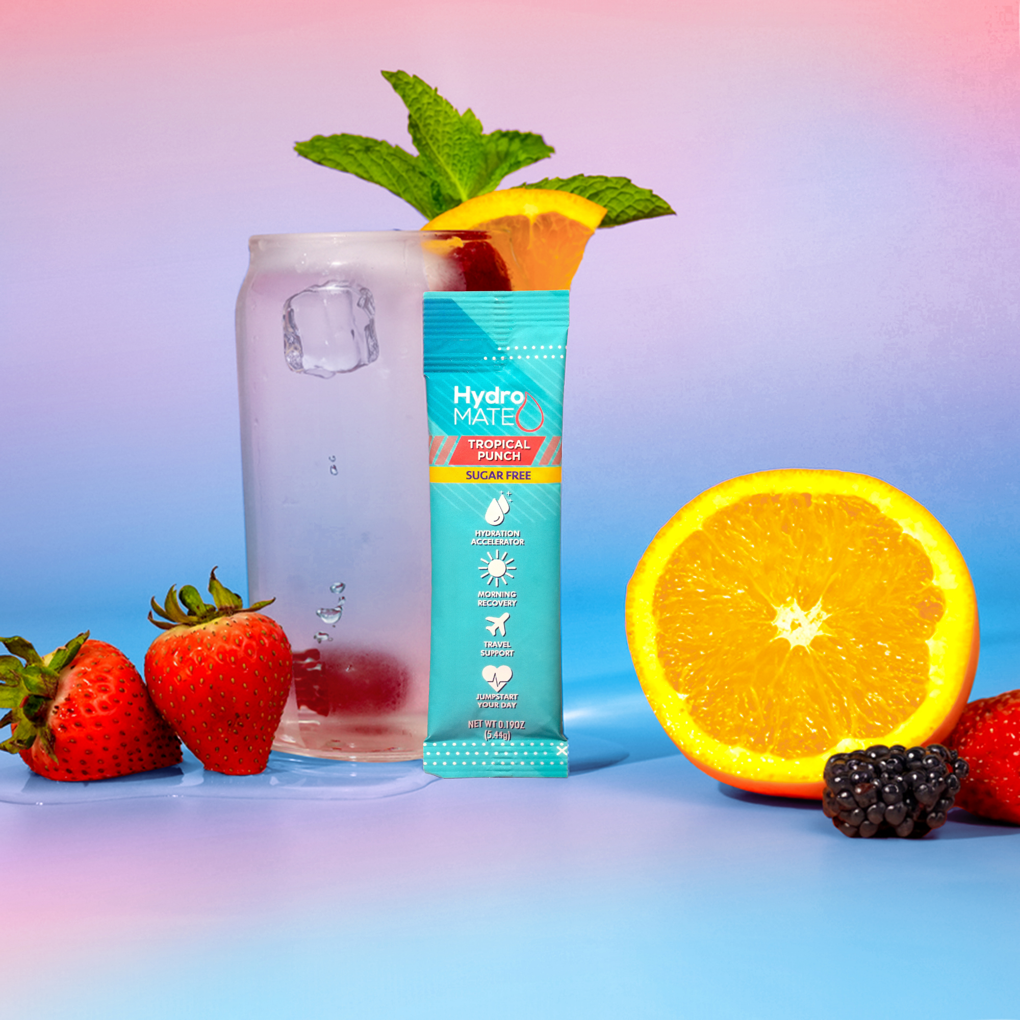 A refreshing Hydro Mate Tropical Punch packet sits beside a glass of ice water, accompanied by fresh strawberries, a sliced orange, blackberries, and a sprig of mint.